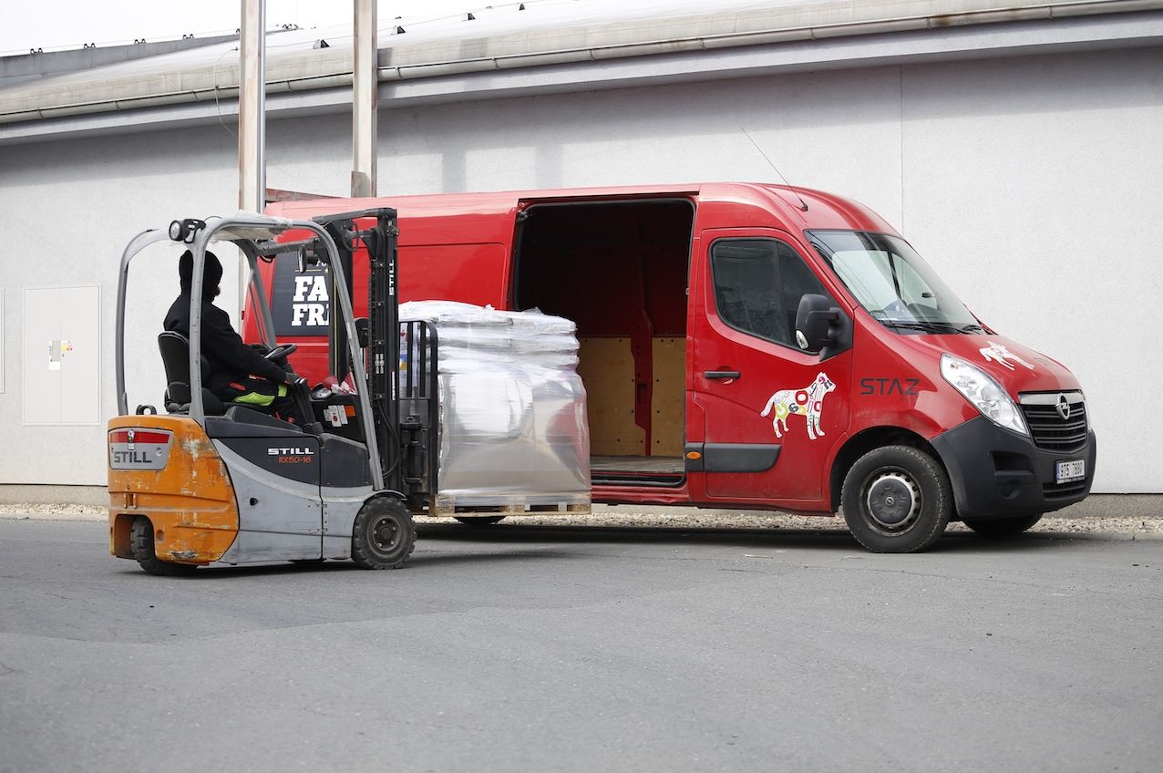A red STAZ van with the dog logo at the warehouse; a forklift is loading a pallet of Farm Fresh food into it